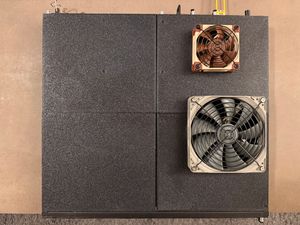 A top-down view of the same switch on a table, with its lid replaced by four custom 3D-printed panels. Two of the panels on the right side have computer case fans mounted externally to the switch, with grilles protecting the exposed side of the fan.